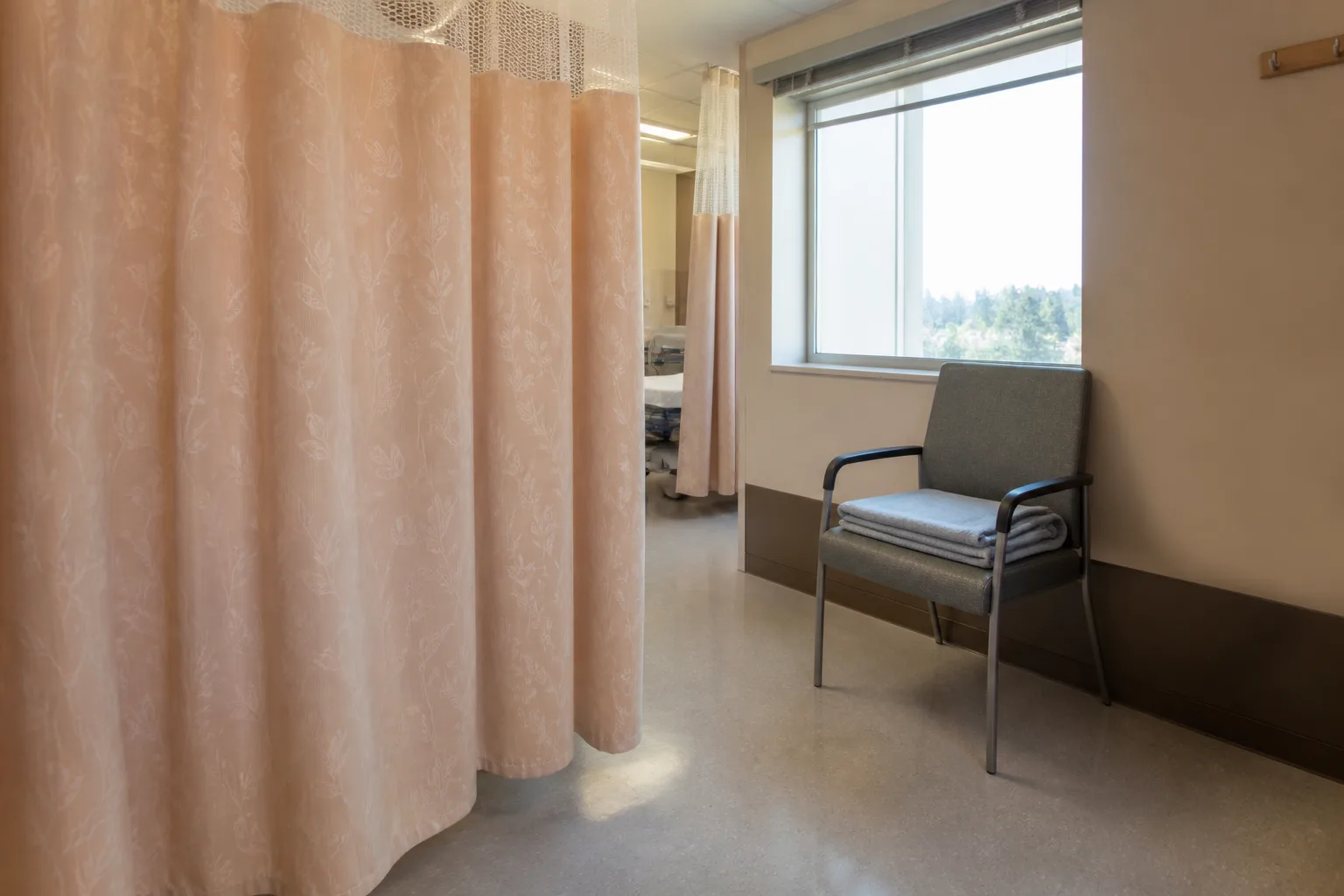 Empty recovery bay with a peach privacy curtain and a visitor chair